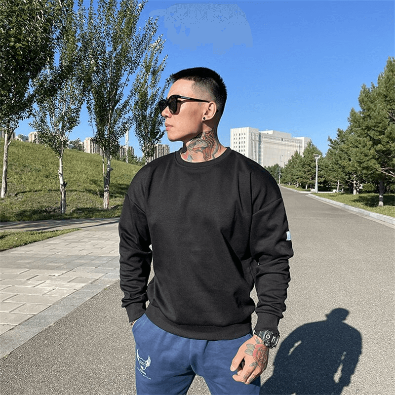 Man wearing loose black sweatshirt with O-neck and full sleeves, standing outdoors. Ideal male activewear for style and comfort.